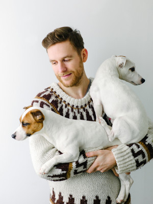 A man in a sweater holding two small dogs in his arms with a pensive look on his face