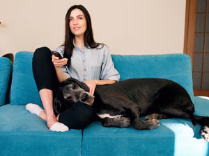 Woman sitting on couch with dog laying on lap watching TV