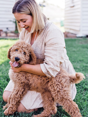 Woman snuggling her small brown doodle dog outside.