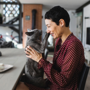 Short haired woman holding a gray cat that's playfully pawing at her nose