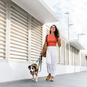 A woman walks along the pavement with a dog on a lead close to her