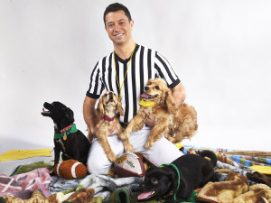 "Puppy Bowl" referee Dan Schachner smiling at camera surrounded by puppies