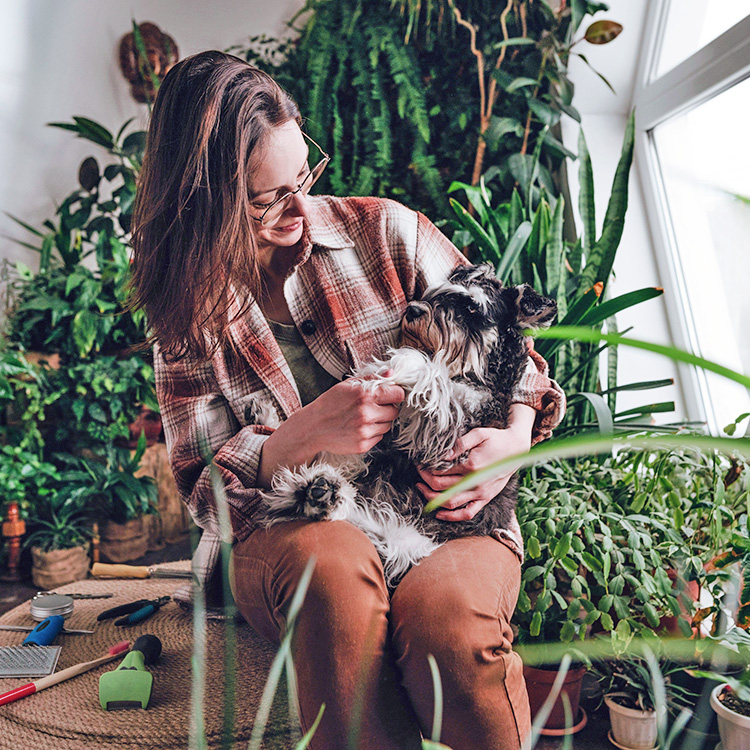 Woman holding her dog on her lap, surrounded by house plants.