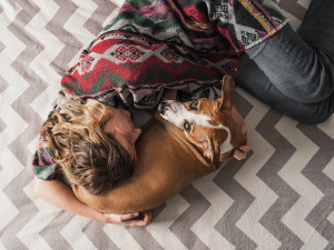 A woman laying on a zig zag patterned blanket while curling around her brown and white dog