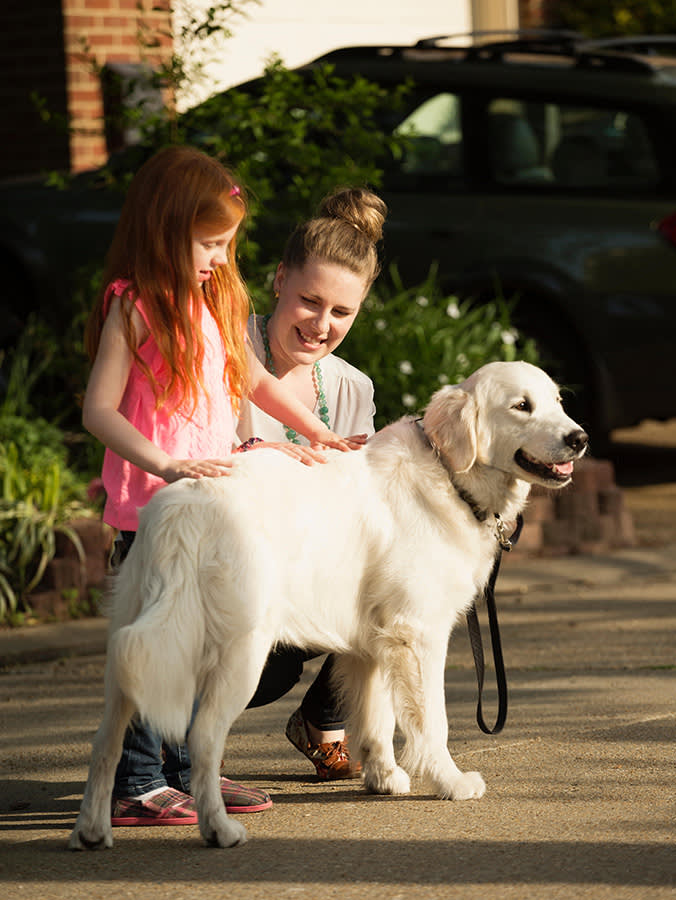 Caucasian mother and daughter petting dog on suburban street.
