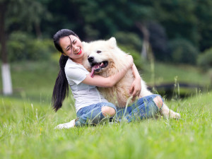 Woman and her large white dog sit in grass outside.