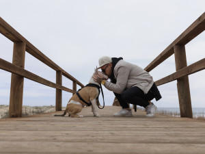 Man kneeling and kissing the head of his white and tan dog on a wooden pier