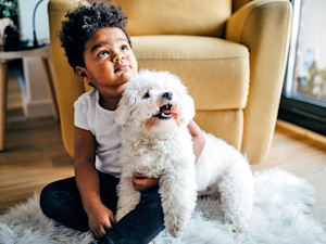 Cute boy cuddling his fluffy white dog at home.