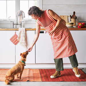 Femme-presenting pet parent feeding their dog a treat in the kitchen