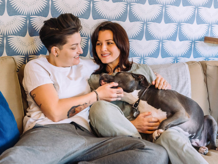 Happy lesbian couple cuddling on the couch with pet dog