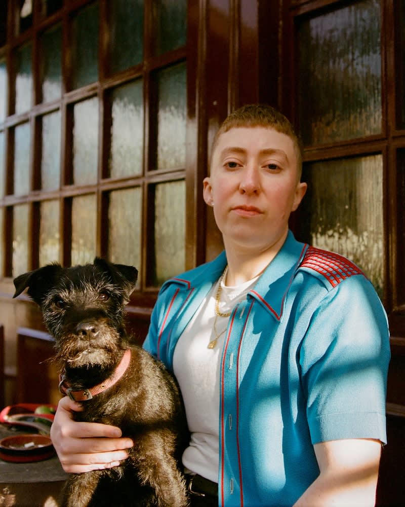 a woman with short cropped hair sits outside a pub holding a dog on her lap