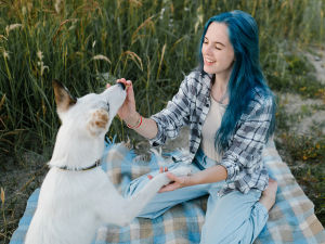 girl with blue hair teaching white dog to shake