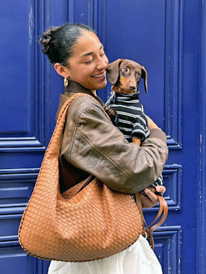 Woman holding her small Dachshund dog in a black and white striped sweater.