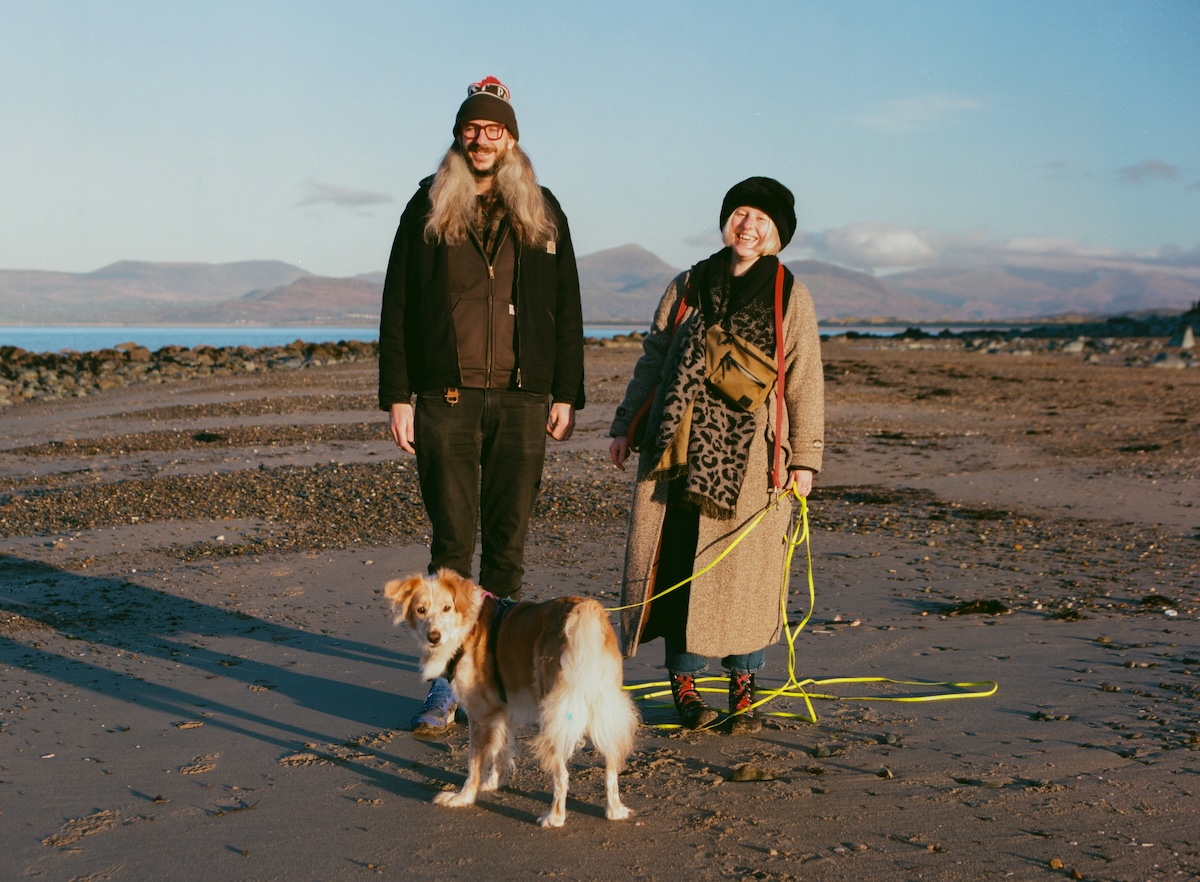 a picture of two people on a beach with a dog at winter