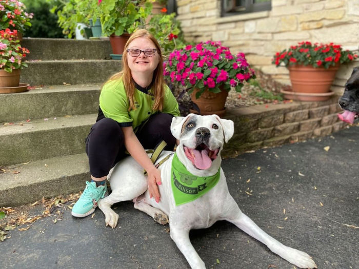 A woman and a dog wearing matching green colors and smiling for a picture. 