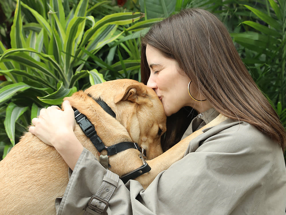 A woman holding her dog close and kissing its head.