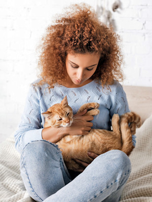 Woman holding her orange cat in her arms in bed.