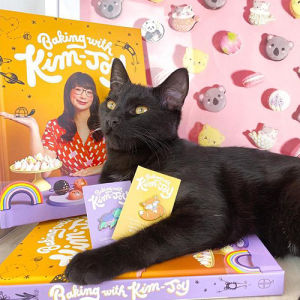 Kim Joy's cat Inki poses with Kim-Joy's new book, Baking With Kim-Joy