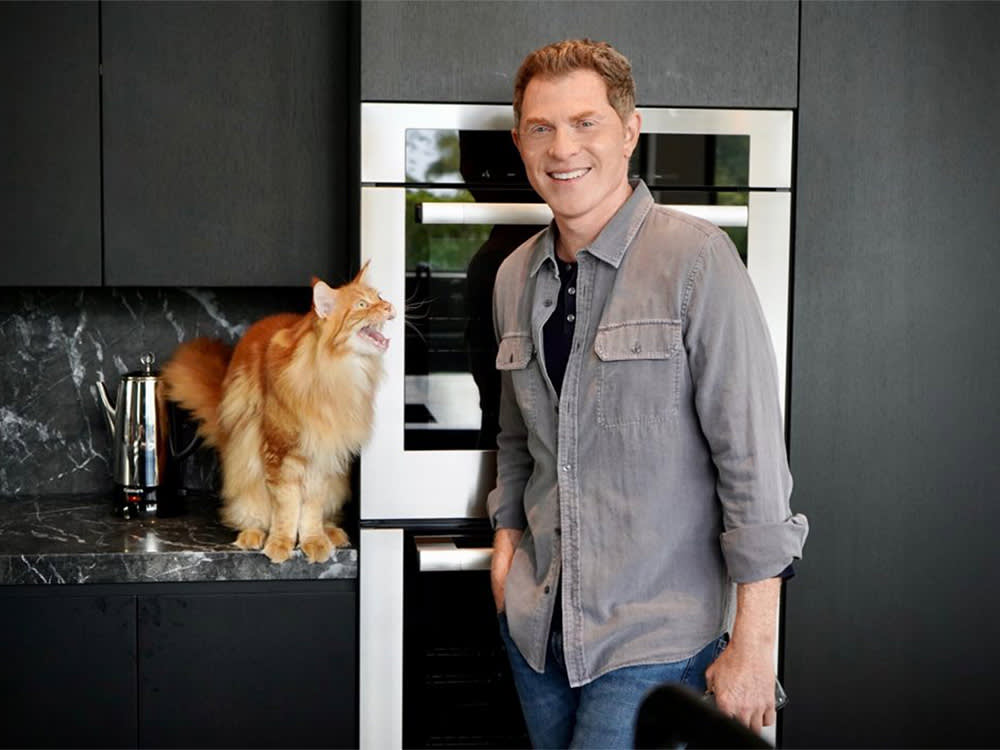 Famous Chef, Bobby Flay posing for a picture in a kitchen with his orange cat. 