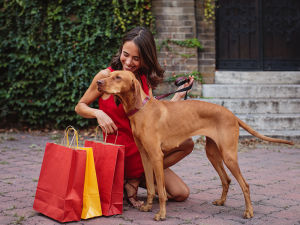 A woman in a red dress holding shopping bags and smiling at her dog.