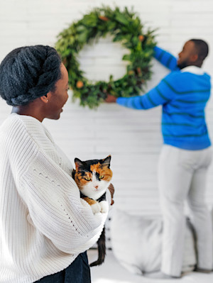 picture of a woman holding a cat while a man puts up a Christmas wreath
