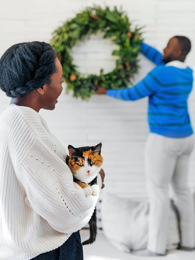 picture of a woman holding a cat while a man puts up a Christmas wreath