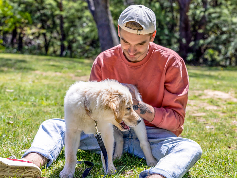 Man petting his puppy's butt outside in the grass.