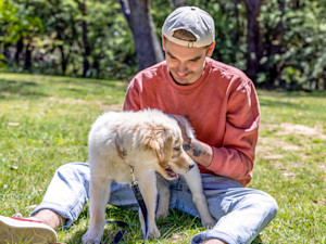 Man petting his puppy's butt outside in the grass.