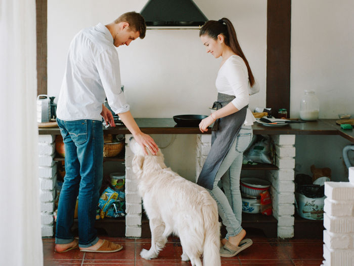 Young couple petting their dog in the kitchen while they make homemade kibble