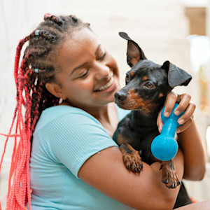 Woman holding her small black dog with his favorite toy.