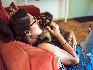 Woman snuggling her cat at home on the couch.