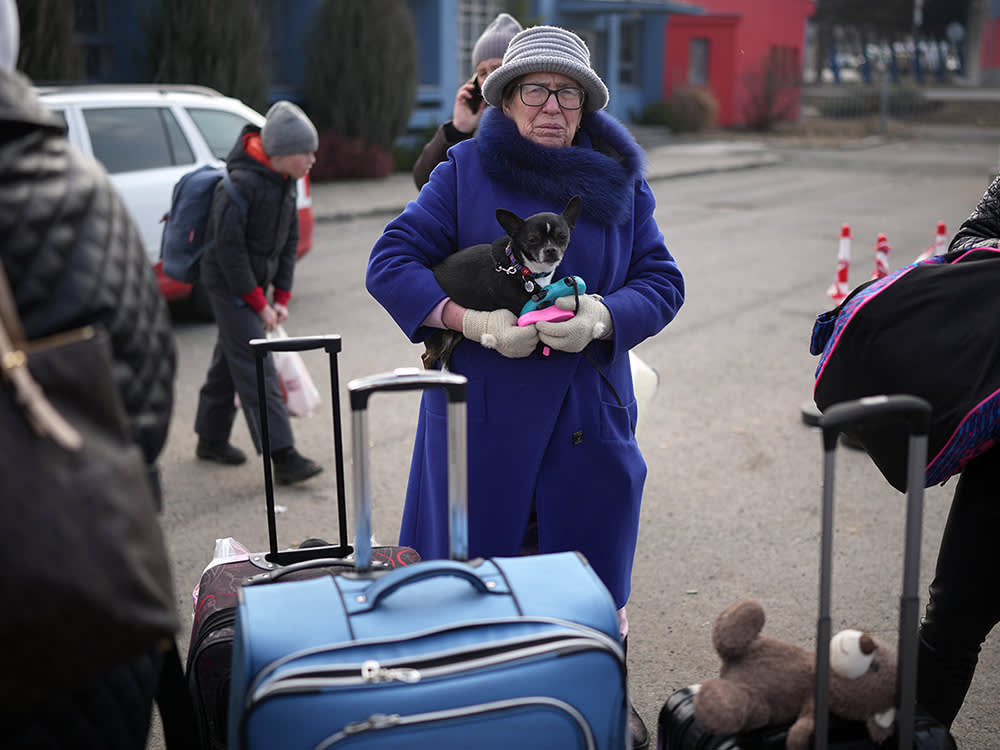 a woman with suitcases holds a small dog 