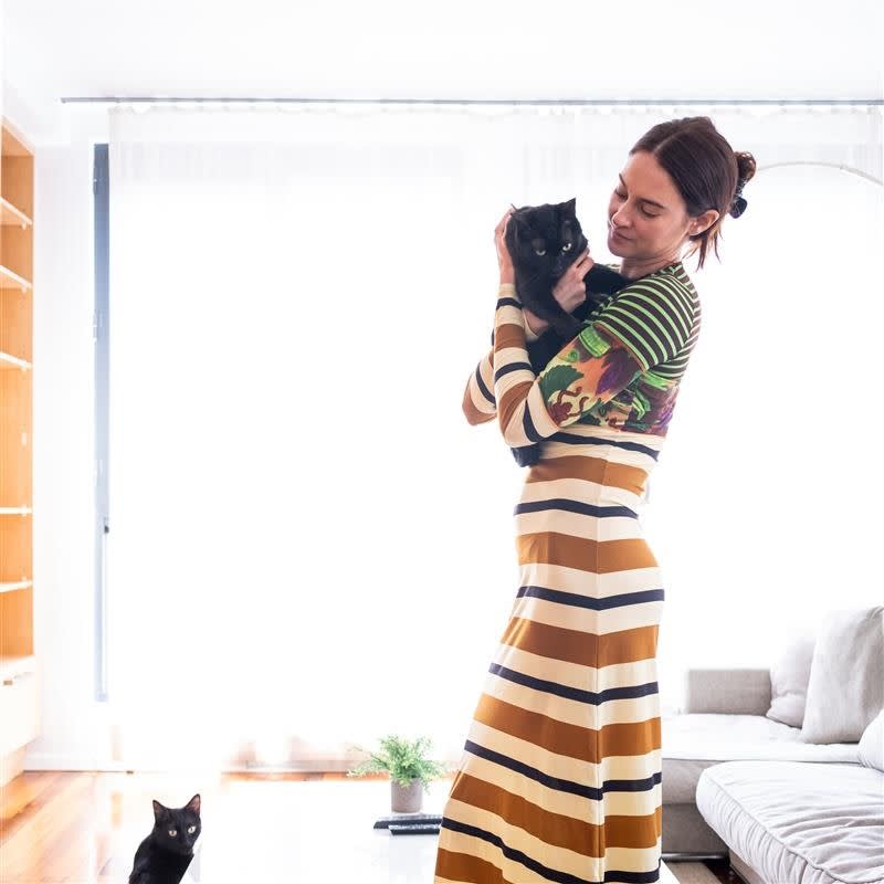 a picture of shailene woodley wearing a striped dress holding a black cat with another black cat at her feet
