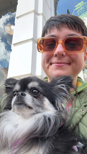 a selfie of a person with short hair wearing orange sunglasses and hugging a small fluffy dog