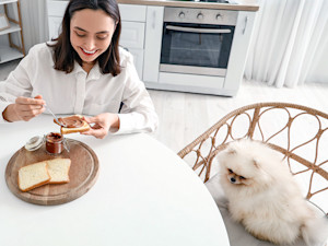 Woman eating Nutella with her dog nearby at home.