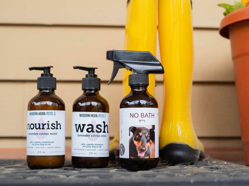 Three bottles of Modern Herb Pet products lined up on a porch next to a pair of yellow rain boots. 