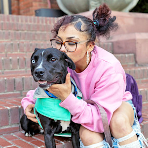 Woman kissing her Pit Bull dog outside.
