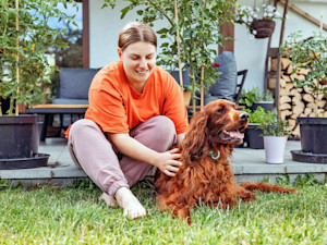 A woman sitting on her patio with her Irish Setter dog on the grass in front of her.