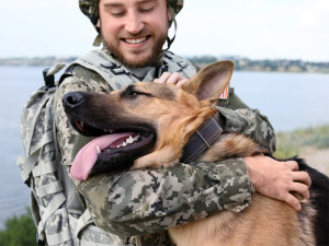 Man in military uniform with German shepherd dog outdoors.