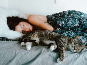 woman with dark hair lying in bed with striped cat, both asleep