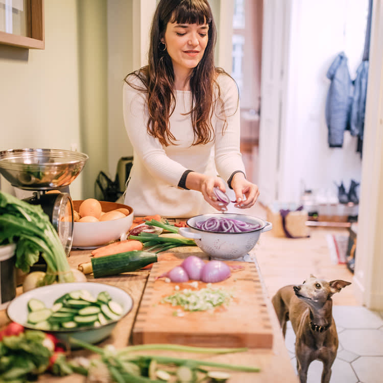 Young woman preparing meal with dog in kitchen.
