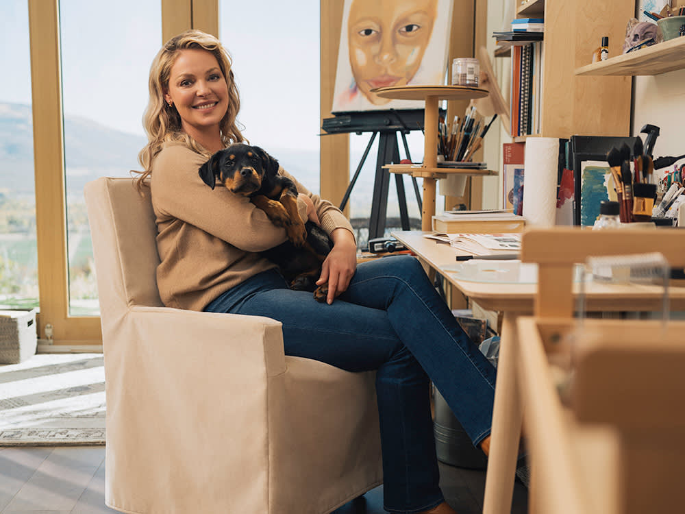 Katherine Heigl snuggles her dog in a chair at her desk.