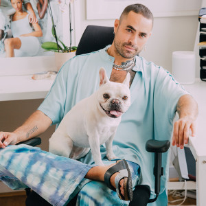 A man in light blue loose clothes with his white Pug dog sitting in his lap