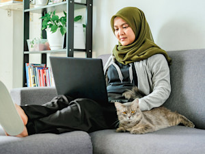 Woman working on a laptop on the couch with her cat.
