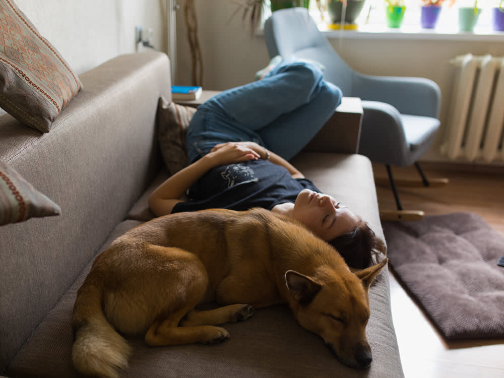 Woman wearing a black t-shirt and jeans laying on the couch with her dog taking a nap