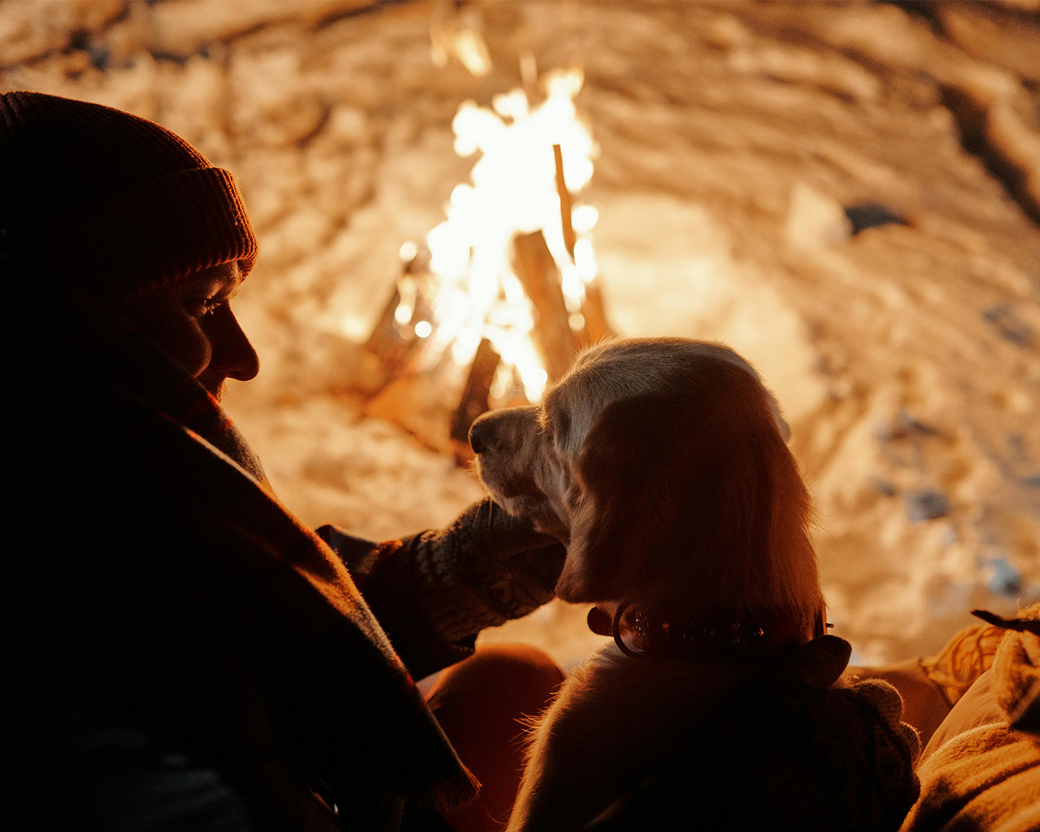 Two people with a dog sat close to a bonfire 