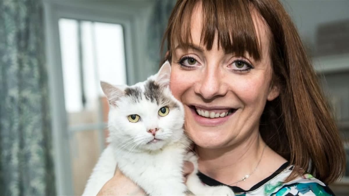 a woman with brown hair and a fringe holds a white cat