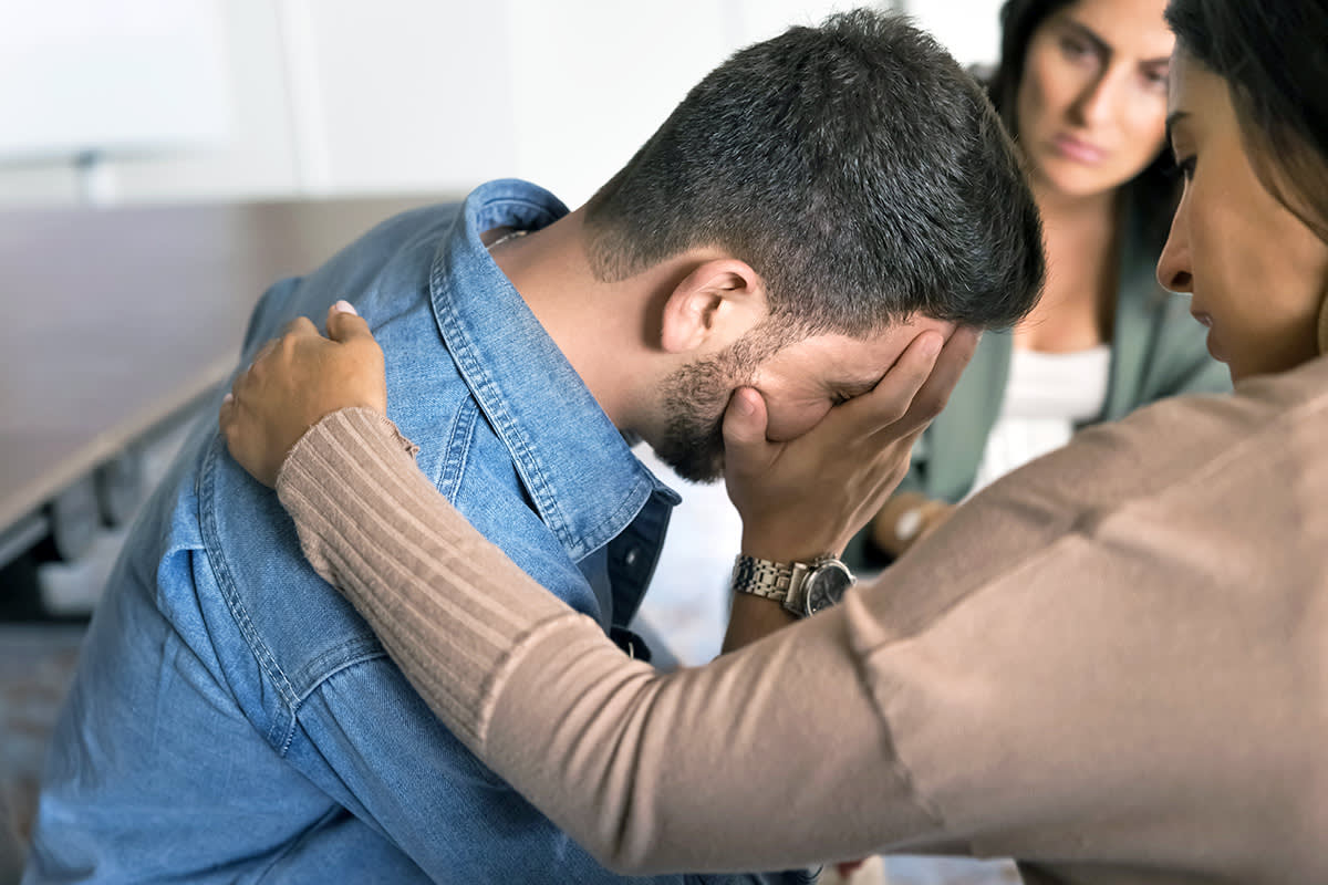 a crying man is consoled by friends