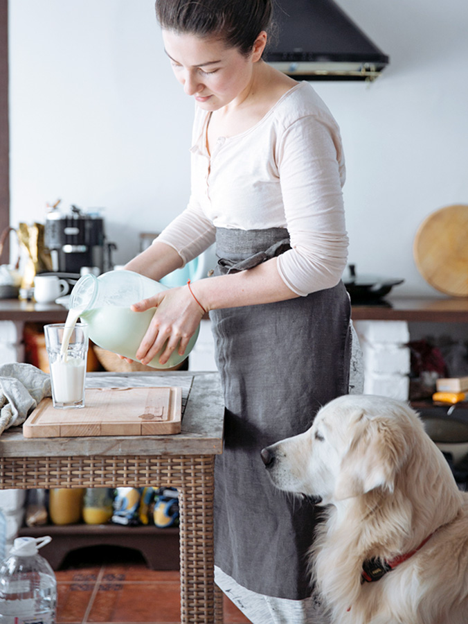 Woman pouring milk into a cup while her Golden Retriever dog watches.