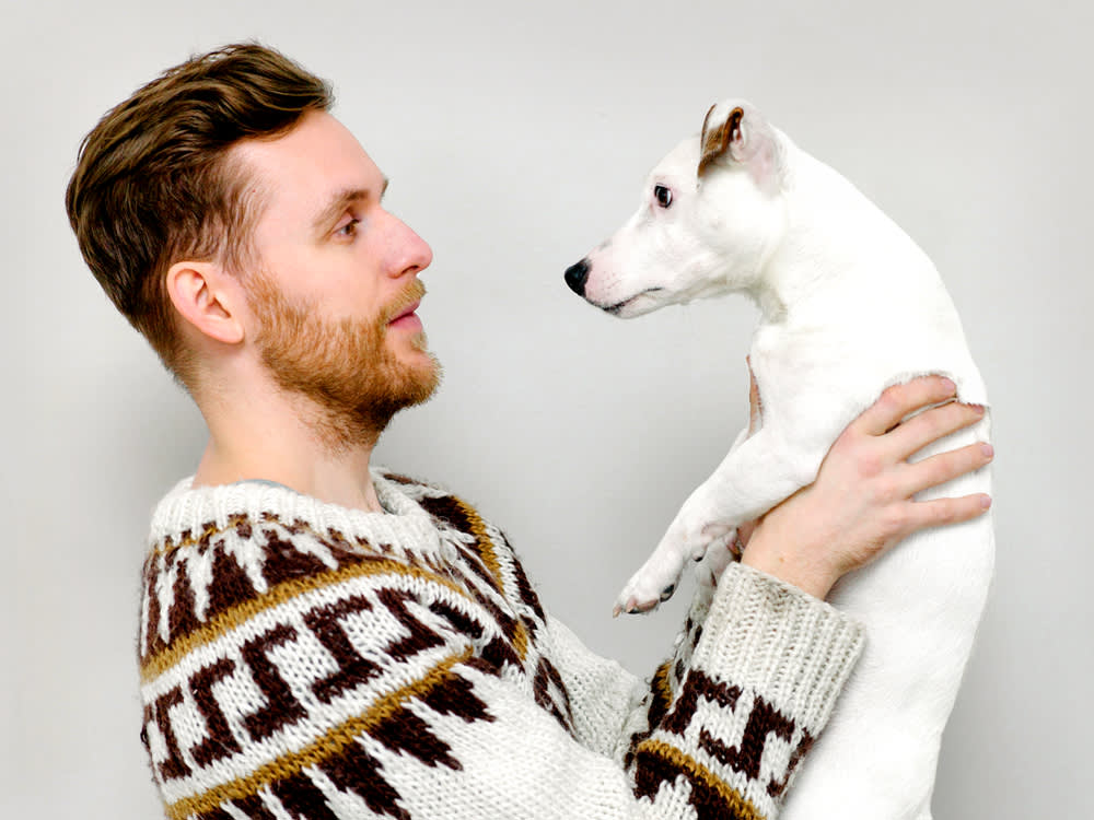 Man holding a dog in front of a light gray background